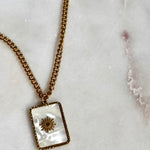 Iridescent Sun Necklace with 18K gold plated stainless steel chain and square sun pendant on marble background