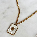 Gold necklace with a rectangular pendant on a marble surface