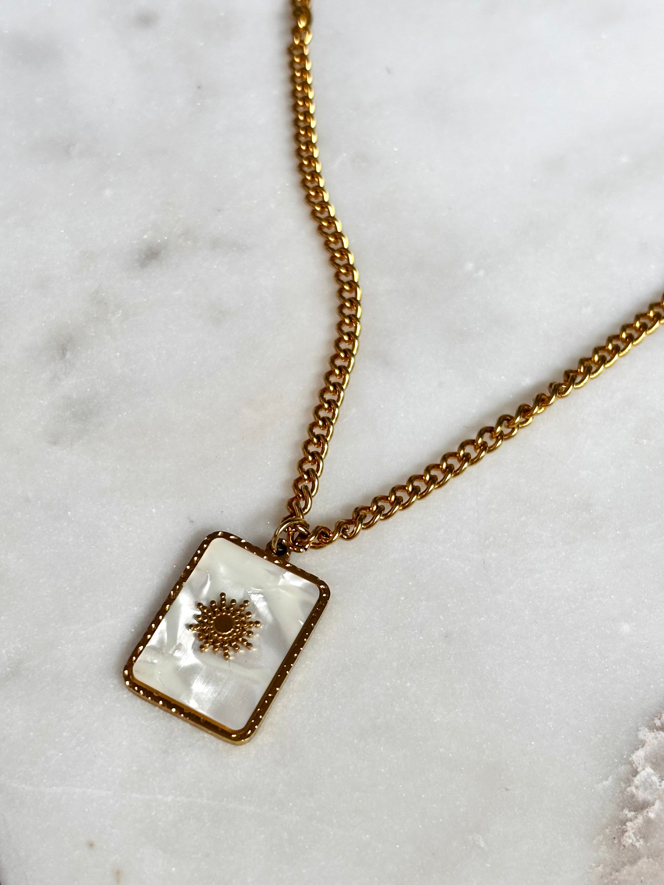 Gold necklace with a rectangular pendant on a marble surface